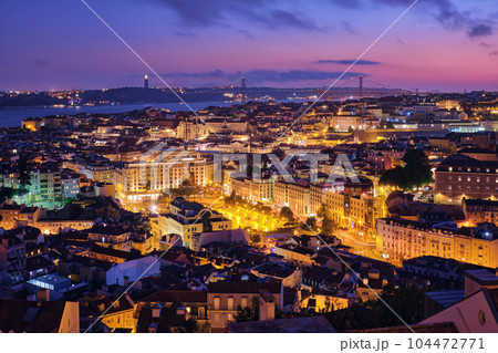 Night view of Lisbon famous view from Miradouro da Senhora do Monte tourist viewpoint of Alfama and Mauraria old city districts, 25th of April Bridge in the evening twilight. Lisbon, Portugal 104472771