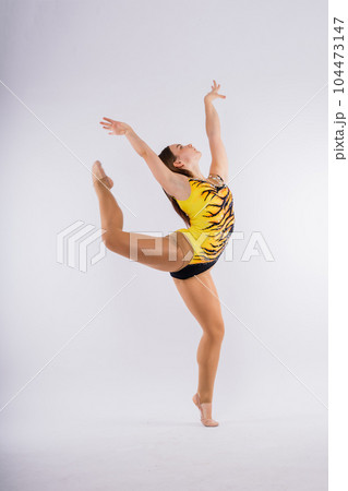 A girl gymnast in a swimsuit does tricks on a white and dark background. Front view 104473147