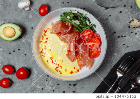 Crepes with fried egg, Jamon slices, fresh tomatoes and cucumber fillings on a white plate on an old wooden table, view from above 104475152