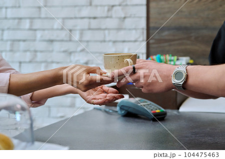 Closeup of hands of barista giving cup of coffee with milk to customer's hands Closeup of hands of barista giving cup of coffee with milk to customer's hands 104475463