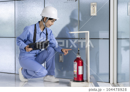 消火器の点検をする作業服の女性　ビルメンテナンス　イメージ 104478928