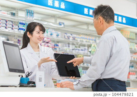 薬局でタブレットPCを使いながら説明する薬剤師・調剤師(レセコン・レセプトコンピュータ) 薬局でタブレットPCを使いながら説明する薬剤師・調剤師(レセコン・レセプトコンピュータ) 104479821