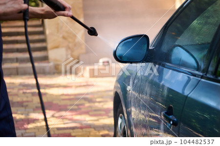 Manual car wash with pressurized water outdoor. Man cleaning, washing vehicle using high pressure water jet in summer. High pressure cleaning equipment, compressor. Car detailing. Hand washer, cleaner Manual car wash with pressurized water outdoor. Man cleaning, washing vehicle using high pressure water jet in summer. High pressure cleaning equipment, compressor. Car detailing. Hand washer, cleaner 104482537
