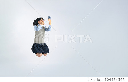 スマホを見ながらジャンプする制服の女子学生 104484565