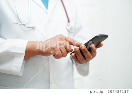 Asian woman doctor holding mobile phone or tablet for search method of treatment patient in hospital. 104487137