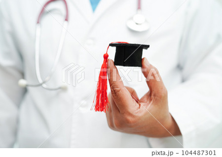 Asian woman doctor holding graduation hat in hospital, Medical education concept. 104487301