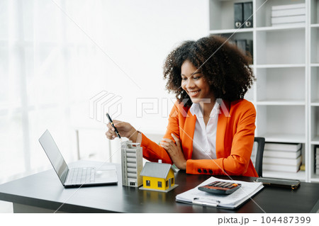 Young real estate agent worker working with laptop and tablet at table in office and small house beside it.. 104487399