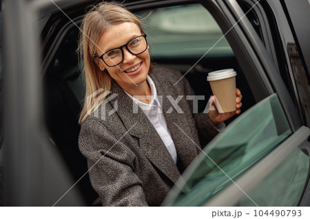 Attractive business woman entrepreneur wearing eyeglasses with takeaway coffee getting out of car Attractive business woman entrepreneur wearing eyeglasses with takeaway coffee getting out of car 104490793