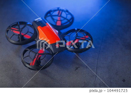 Orange quadcopter mini spy drone on a dark background with blue backlight Orange quadcopter mini spy drone on a dark background with blue backlight 104491725