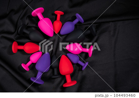 A set of silicone anal plugs in different colors and sizes on a black silk sheet.  104493460