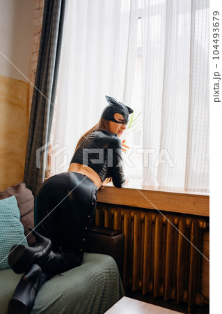 Playful attractive sexy young woman in black leather cat suit on the couch 104493679