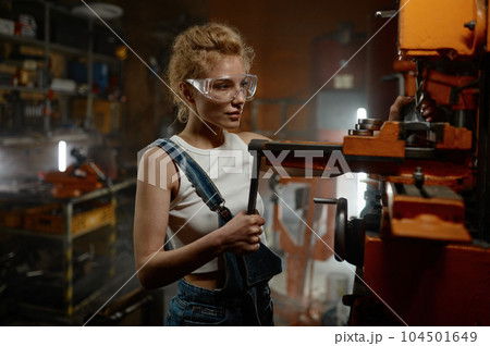 Woman wearing safety protective goggles working on milling and drilling machine Woman wearing safety protective goggles working on milling and drilling machine 104501649
