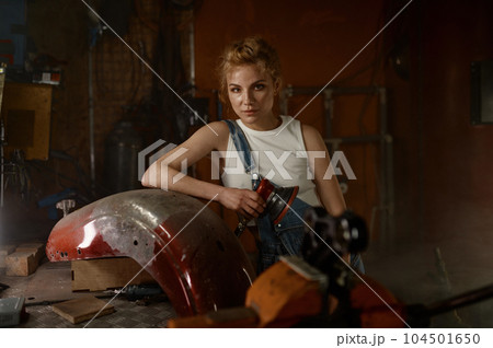 Young woman doing hard job at motorcycle garage using grinder 104501650