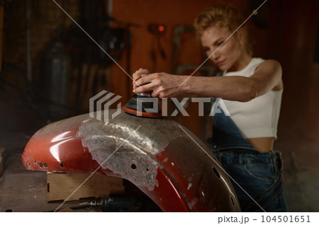 Young woman doing hard job at motorcycle garage using grinder 104501651