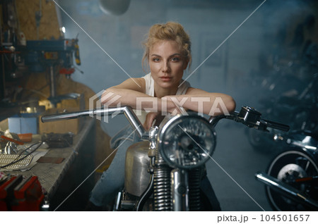 Portrait of beautiful woman biker sitting on motorcycle in garage 104501657