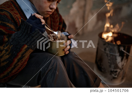 Poor homeless woman eating preserved canned food while warming at bonfire 104501706