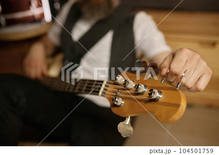 Bearded brutal guitarist tuning his musical instrument while sitting on floor Bearded brutal guitarist tuning his musical instrument while sitting on floor 104501759