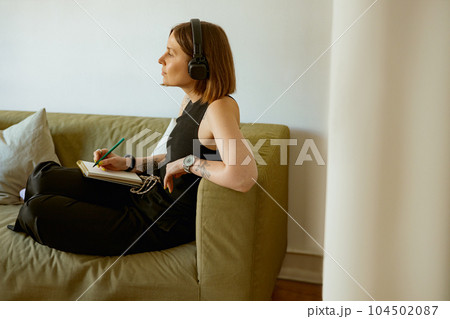 Female student listening webinar in headphones and making notes at home. Distance learning concept 104502087