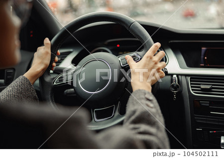 Back view of woman driver pushes the button on steering wheel during drive 104502111