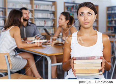 Tired girl sitting with pile of books in high school library 104503500