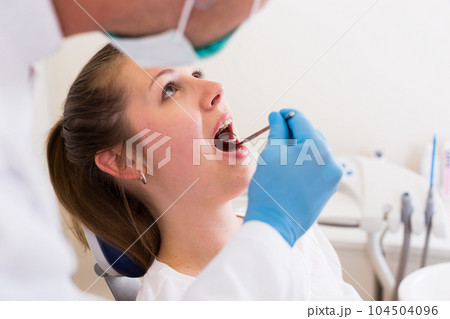 Young doctor in white is taking examination of a woman on the chair 104504096