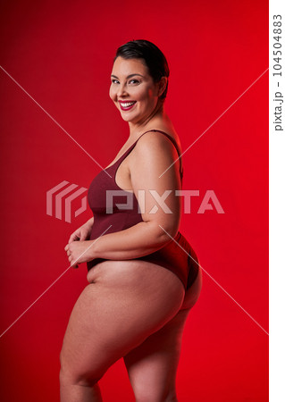 Half-turned smiling lady in underwear standing over red studio background Half-turned smiling lady in underwear standing over red studio background 104504883