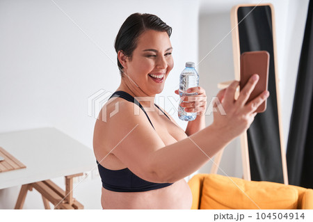 Woman holding her smartphone and bottle of water while video calling Woman holding her smartphone and bottle of water while video calling 104504914