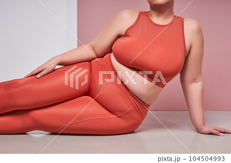 Cropped view of the full figured woman sitting against pink studio background Cropped view of the full figured woman sitting against pink studio background 104504993