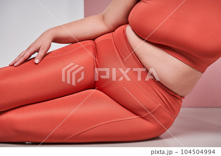 Cropped view of the full figured woman sitting against pink studio background Cropped view of the full figured woman sitting against pink studio background 104504994