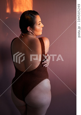 Back view of body positive black lady posing, hugging her bare shoulder 104505249