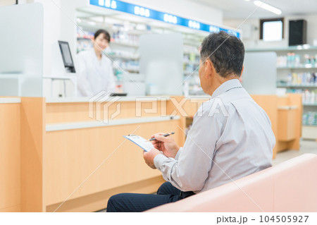 病院・薬局の待合室で問診票を書く高齢者男性と薬剤師 病院・薬局の待合室で問診票を書く高齢者男性と薬剤師 104505927