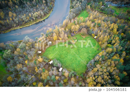 This photo features a heart-shaped lawn in the middle of an autumn forest, located near a river. The image was captured on a cloudy day, adding a moody and atmospheric feel to the scene. 104506181