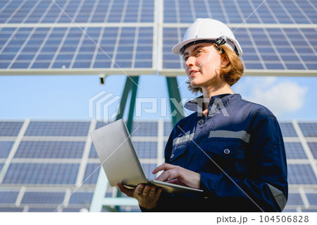 Female engineer holding laptop checking solar panels at solar farm 104506828