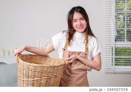 Female housekeeper cleaner taking messy dirty clothes on sofa into basket Female housekeeper cleaner taking messy dirty clothes on sofa into basket 104507359
