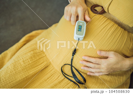 Pregnant woman with pulse oximeter on finger. Doctor measuring oxygen saturation level while visiting expectant mother with coronavirus disease at home, cropped. Pregnancy and covid-19 concept Pregnant woman with pulse oximeter on finger. Doctor measuring oxygen saturation level while visiting expectant mother with coronavirus disease at home, cropped. Pregnancy and covid-19 concept 104508630