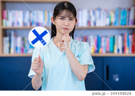 バツのプレートを出す看護師の女性 104509026