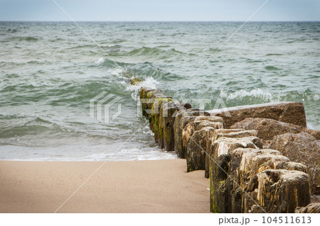Landscape of beach and wooden breakwaters with sea waves. Stormy day at sea Landscape of beach and wooden breakwaters with sea waves. Stormy day at sea 104511613