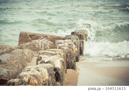 Vintage wooden breakwaters and sea waves at beach. Windy day at sea. Travel and tourism. Vintage wooden breakwaters and sea waves at beach. Windy day at sea. Travel and tourism. 104511615