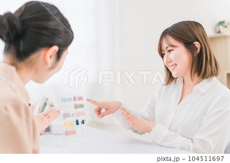 ネイルサロンでネイルチップを見てデザインを選ぶ女性と説明するネイリスト 104511697