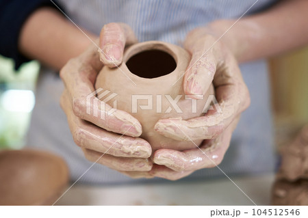woman forming clay pot shape by hands, closeup in artistic studio 104512546