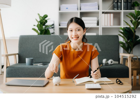 Asian women's hand saving a coin into piggy bank with wooden to calculateon and tablet on the table for business, finance, saving money and property investment concept. Asian women's hand saving a coin into piggy bank with wooden to calculateon and tablet on the table for business, finance, saving money and property investment concept. 104515292