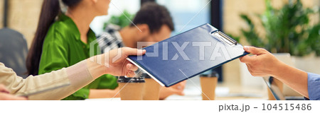 Male coworker giving a folder with documents to his colleague while working in the modern office 104515486