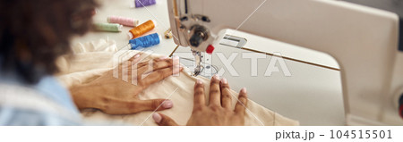 African-American worker sews white fabric with machine tool at t 104515501