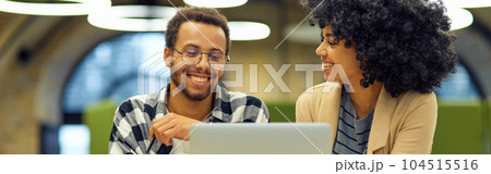 Two young happy multiracial business people sitting at the desk in the modern office, using laptop and discussing project, man and woman working together in coworking space Two young happy multiracial business people sitting at the desk in the modern office, using laptop and discussing project, man and woman working together in coworking space 104515516