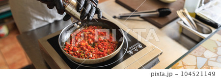 Close up of professional chef in uniform adds spices into pan with dish in restaurant kitchen Close up of professional chef in uniform adds spices into pan with dish in restaurant kitchen 104521149