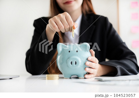 Asian woman putting coin into piggy bank. Saving money with coins Step into a business that is growing to be successful and save for retirement concepts Asian woman putting coin into piggy bank. Saving money with coins Step into a business that is growing to be successful and save for retirement concepts 104523057