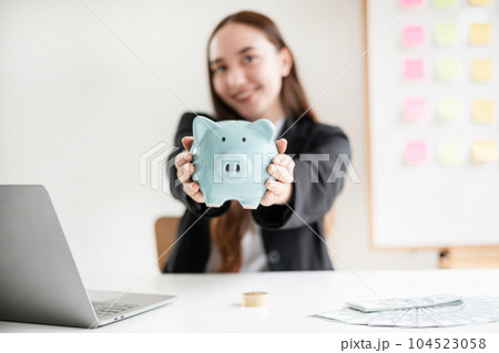 Asian woman putting coin into piggy bank. Saving money with coins Step into a business that is growing to be successful and save for retirement concepts Asian woman putting coin into piggy bank. Saving money with coins Step into a business that is growing to be successful and save for retirement concepts 104523058