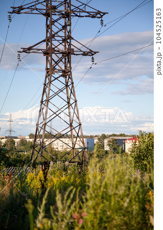 Transmission tower in the green field providing electricity supply for a town. Beautiful landscape with a pylon of a power line in the field among wild plants and grass Transmission tower in the green field providing electricity supply for a town. Beautiful landscape with a pylon of a power line in the field among wild plants and grass 104525163