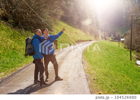 Two hikers are in the mountains in the spring nature outdoor. Hiking with backpacks. Two friends travel together in picturesque places. The man shows the way. Two men on a hiking trip in the mountains 104526980