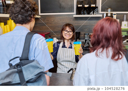 Female coffee shop worker serving customers giving paper cups of takeaway coffee Female coffee shop worker serving customers giving paper cups of takeaway coffee 104528276